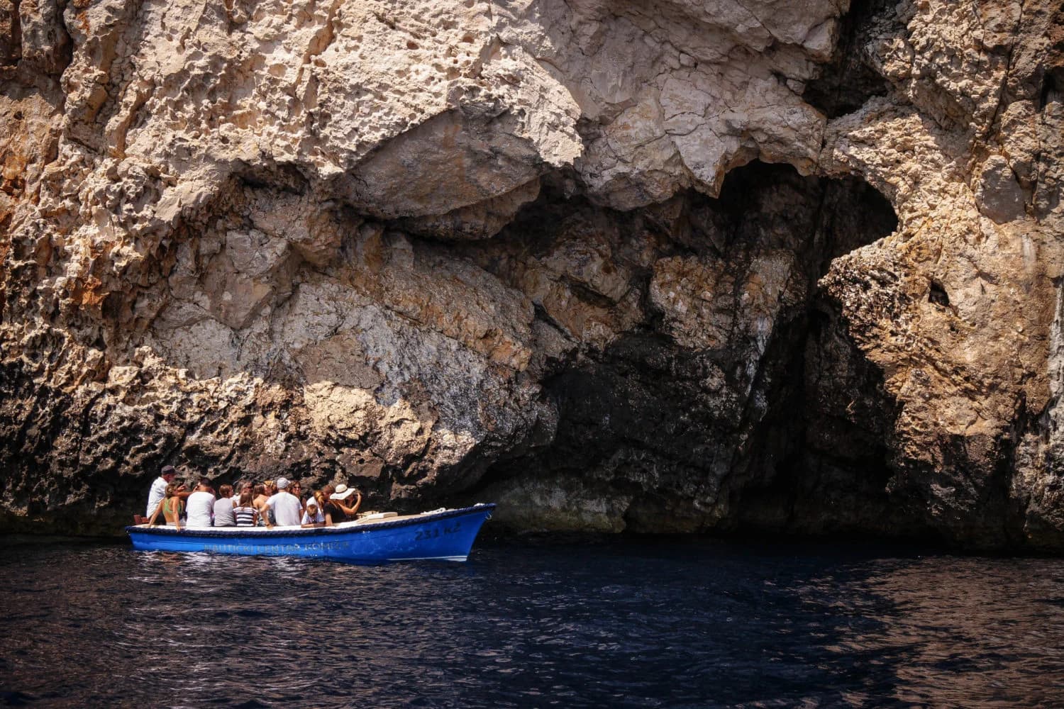 A wooden boat of visitors inside the Blue Cave, lit by the blue water beneath it (Blå Grottan – Privat tur)