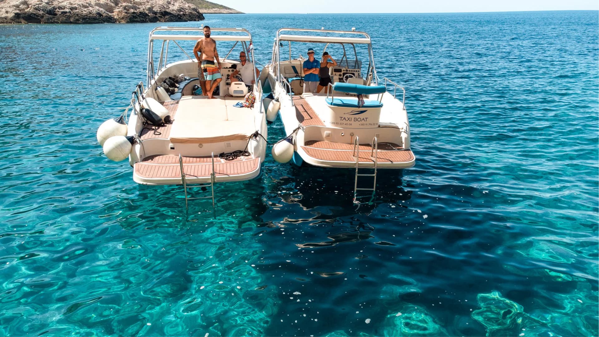 Two speedboats rafted together at a swim stop, guests on deck over clear water